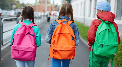 3 niñas y niños de espaldas con mochilas